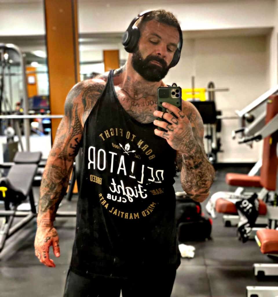 Un uomo che esegue esercizi di MMA in palestra mentre scatta un selfie con il telefono.