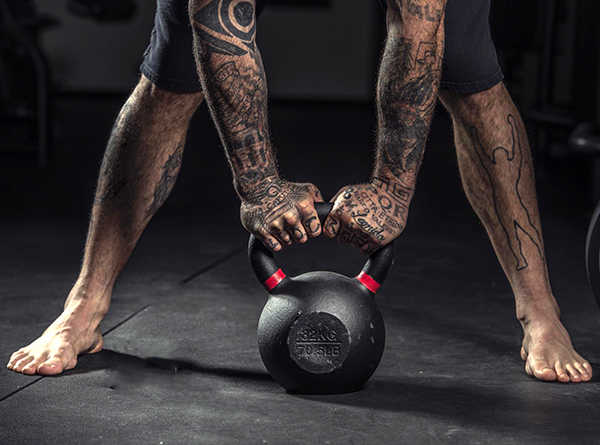 Un uomo che si allena con tatuaggi che solleva un kettlebell in palestra.