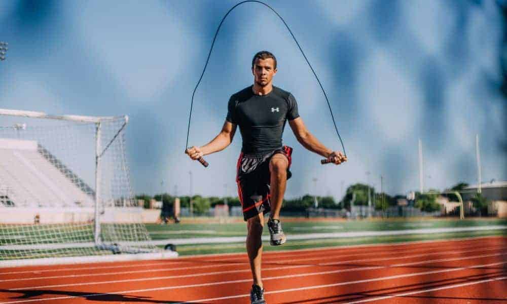 Un uomo che esegue esercizi di gioco di gambe con una corda per saltare su una pista.