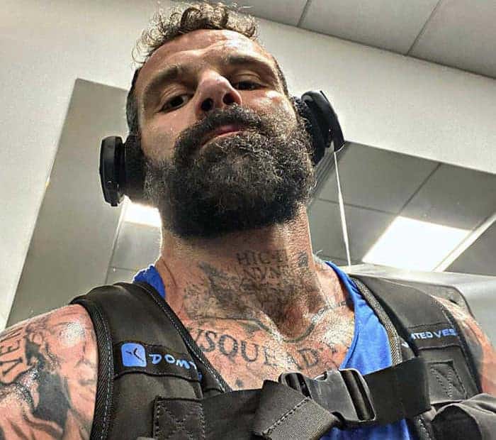 Un uomo barbuto con tatuaggi si fa un selfie.