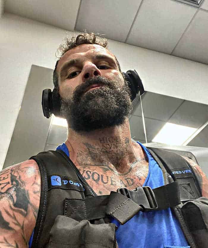 Un uomo barbuto con tatuaggi si fa un selfie.