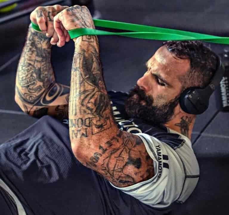 Un uomo con tatuaggi che partecipa al programma di 10 settimane del LEGIONARIO FIGHT CAMP durante la prima settimana su una fascia di resistenza verde.