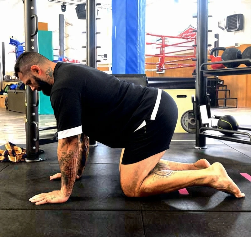 Uomo con tatuaggi in posizione di quadrupedia in palestra